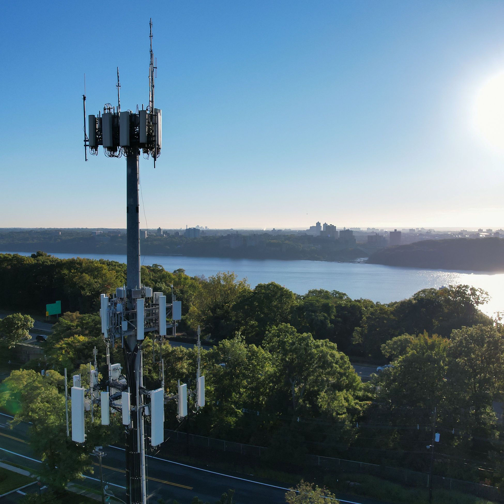 A tall telecommunications tower with antennas overlooking a river and city skyline.